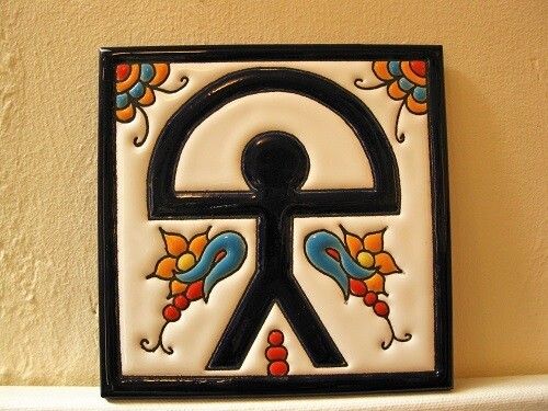 A decorative ceramic tile features a stylized black stick figure with a semicircle above its head, surrounded by colorful floral and paisley patterns on a white background.