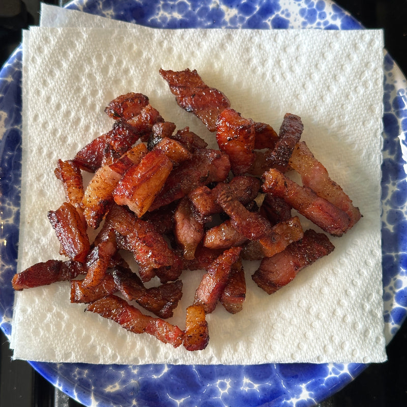 A pile of crispy, browned bacon strips sits on a paper towel on top of a blue and white speckled plate.