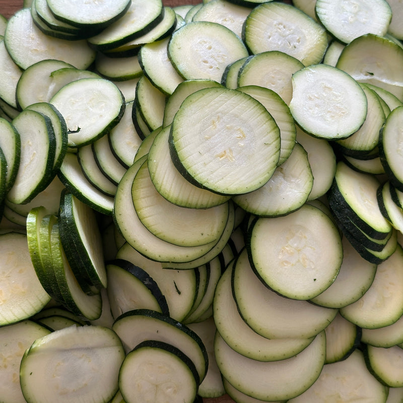 A close-up of many slices of fresh zucchini, showing the light green interiors and dark green edges, arranged in overlapping layers.