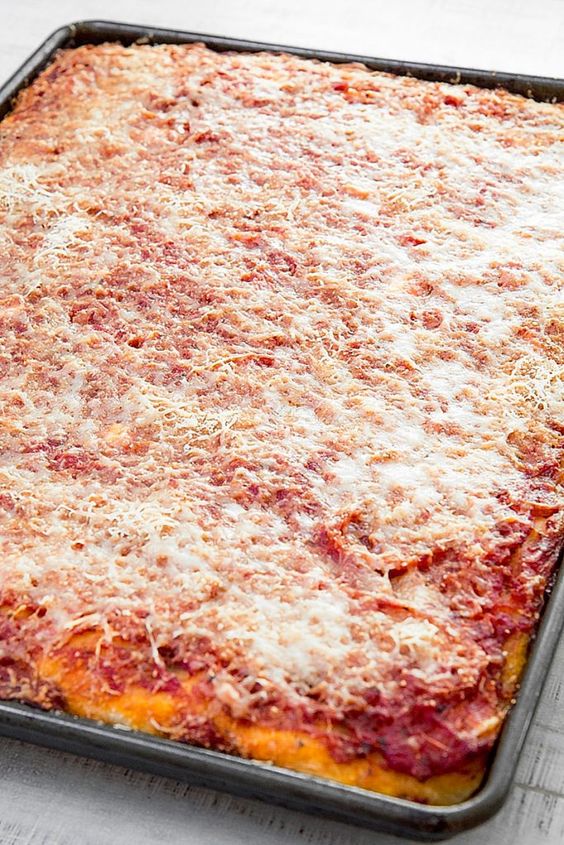A rectangular sheet pan pizza with a thick, golden crust, topped with tomato sauce and melted cheese, fills the entire baking tray. The pizza has a rustic, homemade appearance.
