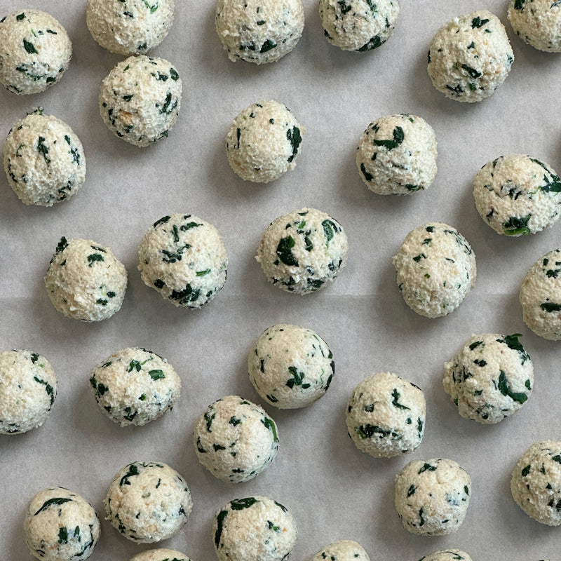 Dozens of uncooked spinach and ricotta dumplings arranged in neat rows on parchment paper, viewed from above.
