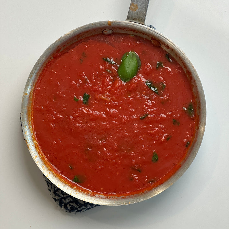 A pan filled with red tomato sauce, garnished with fresh basil leaves, sits on a white surface.