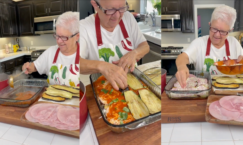 A woman in glasses and a vegetable-print apron prepares an eggplant and ham lasagna, layering sauce, eggplant slices, ham, and cheese in a glass baking dish on a wooden board in a modern kitchen.