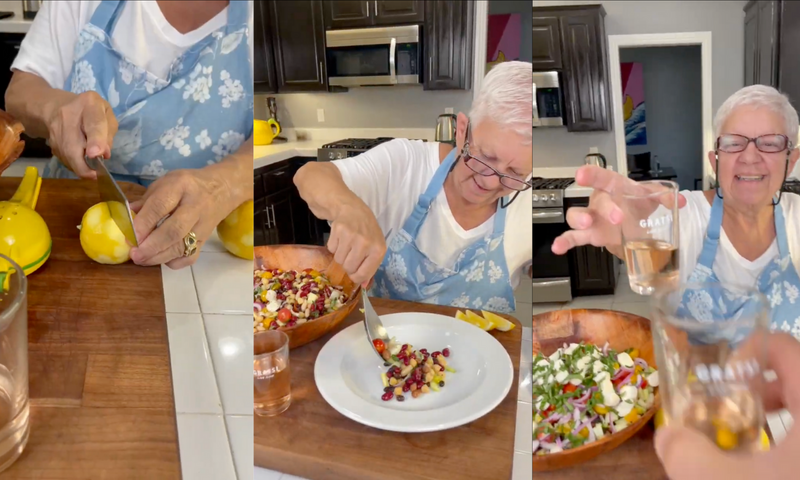 A woman in a blue apron slices a lemon, prepares a colorful salad with pomegranate seeds, and holds up a small glass in a bright kitchen.