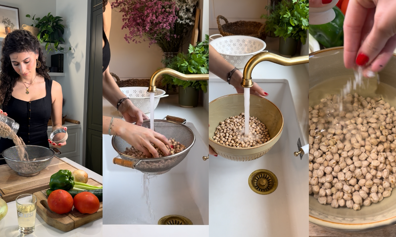 A woman prepares chickpeas by pouring them into a colander, rinsing them under running water, and sprinkling salt over them, with vegetables and kitchen items visible nearby.