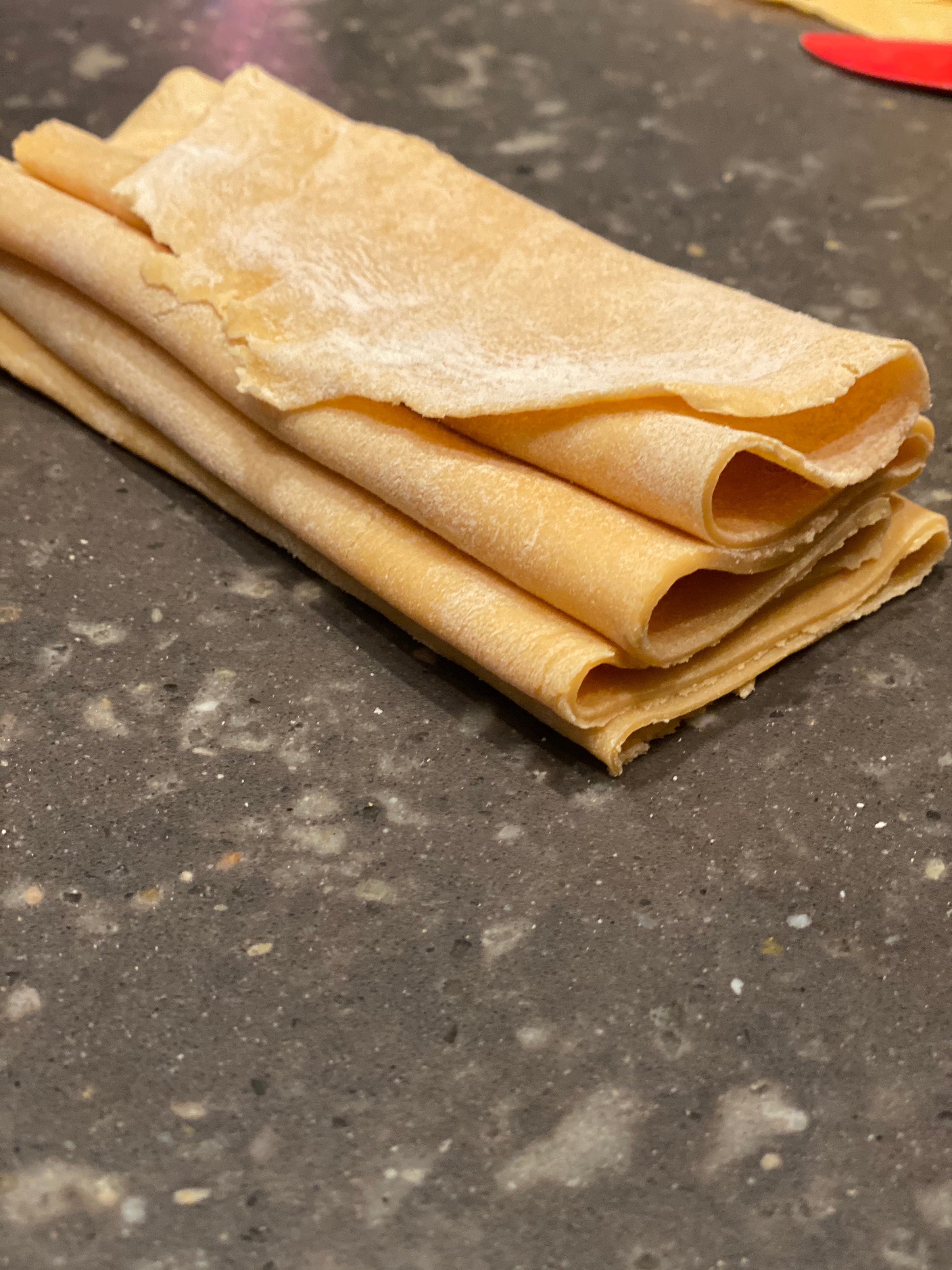 A close-up of several folded sheets of uncooked pasta dough resting on a speckled gray countertop.
