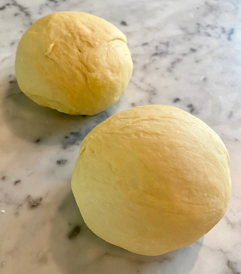 Two smooth, round balls of dough rest on a marbled countertop, ready for baking or further preparation.