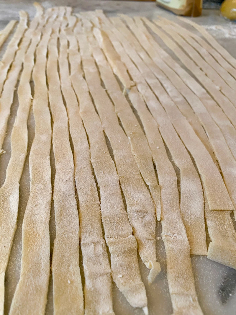 Rows of freshly cut, uncooked pasta noodles are spread out on a floured surface, ready to be cooked or dried.