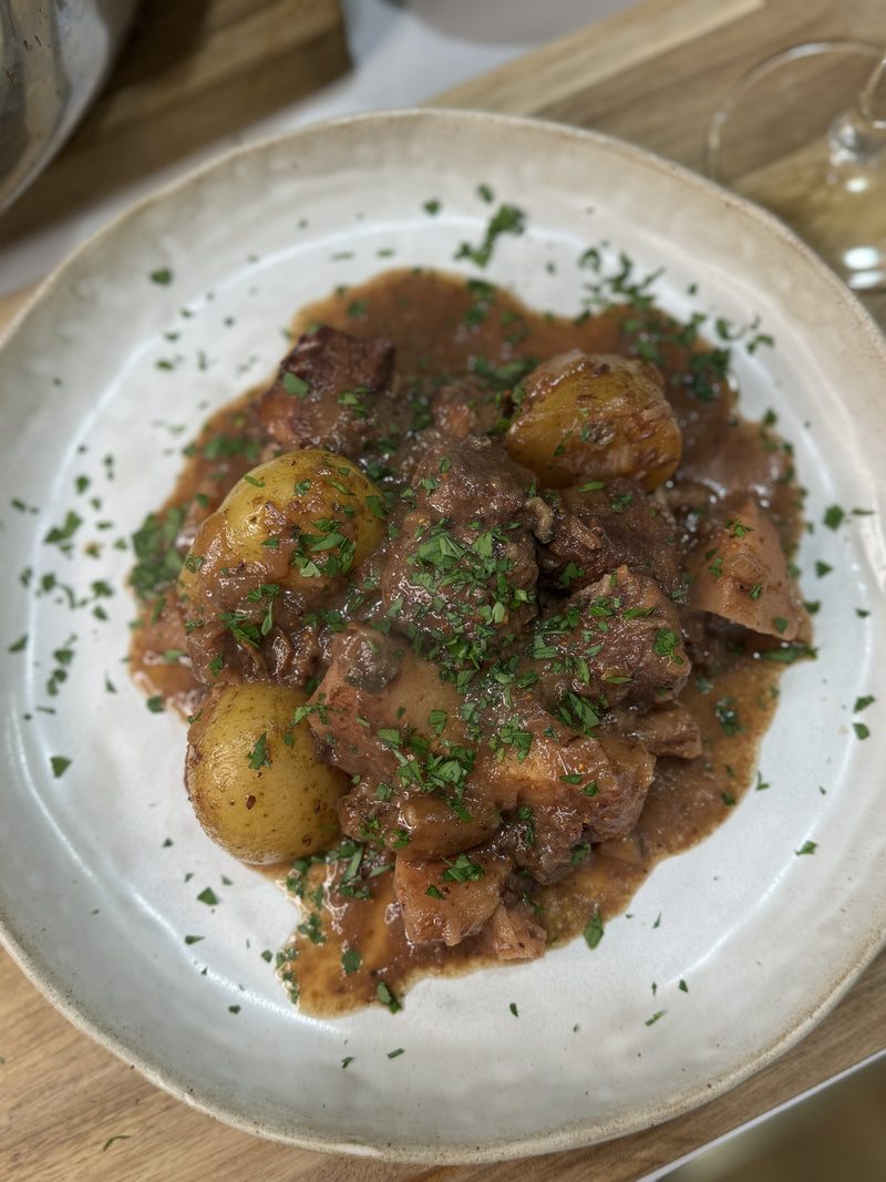 A plate of beef stew with potatoes and carrots in a rich brown sauce, garnished with chopped fresh herbs, served on a white ceramic dish.