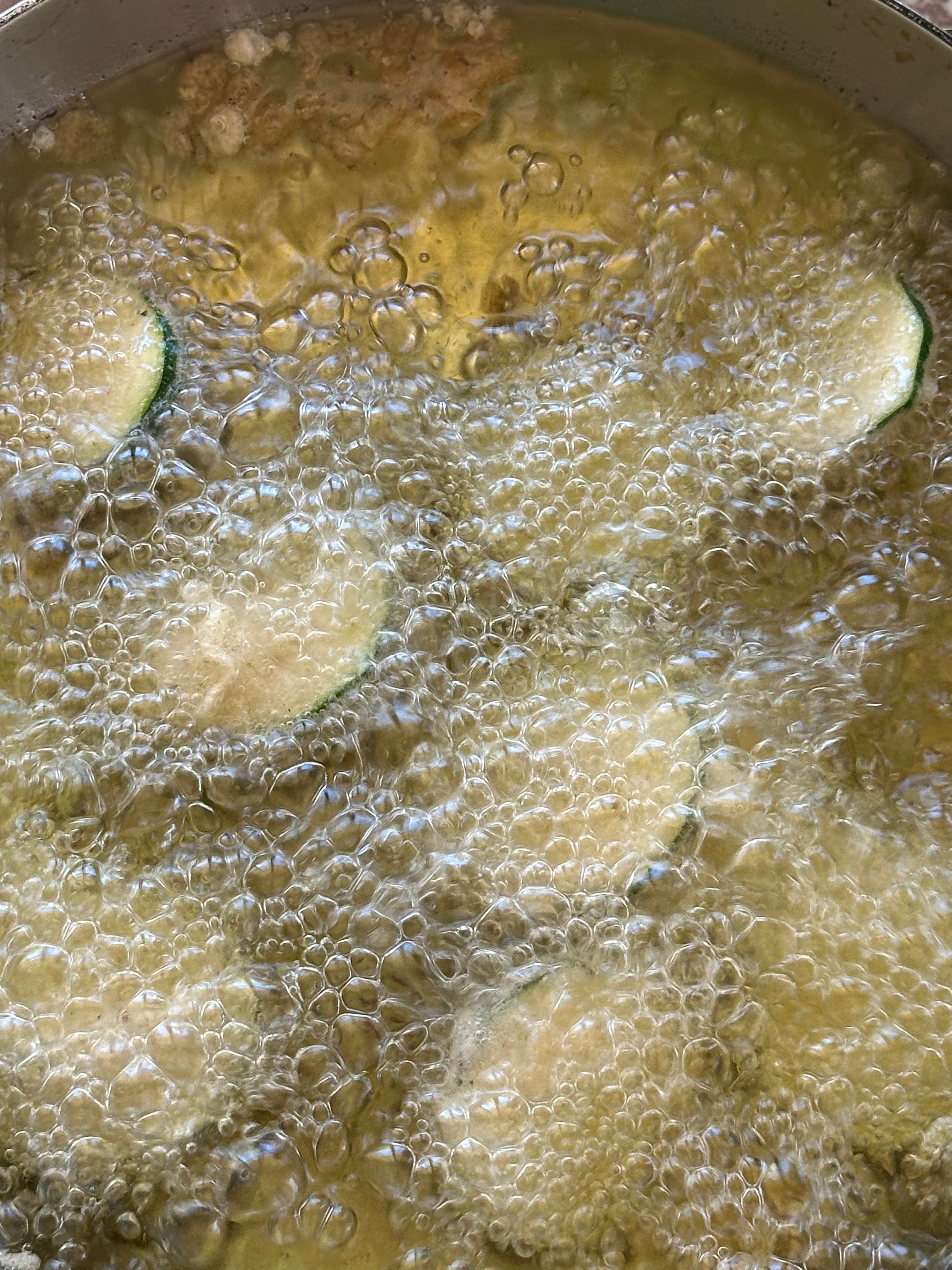 Sliced zucchini rounds frying in hot oil, surrounded by bubbling and sizzling, as they cook in a pan.