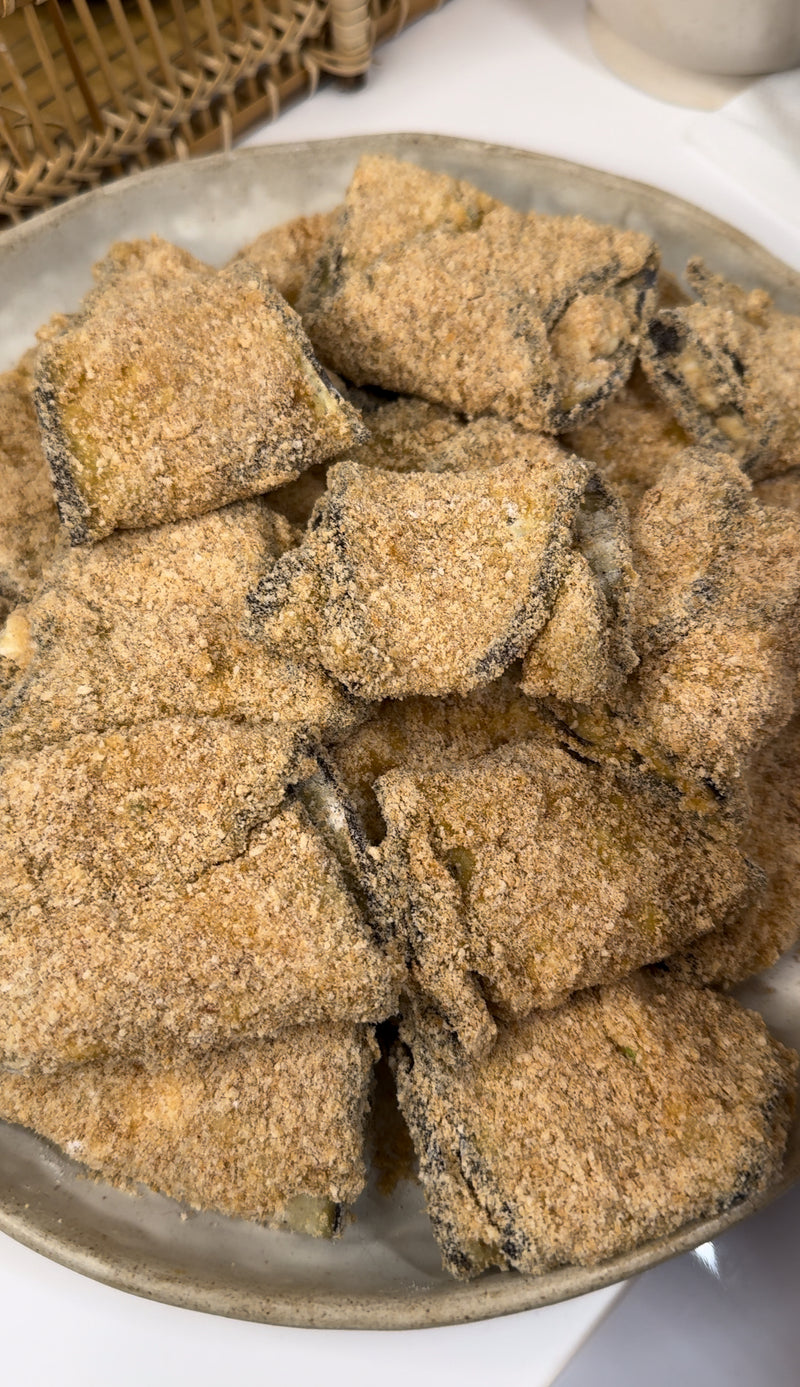 A plate filled with breaded rectangular pieces of food, likely fried or ready to be fried, each piece appears to have a dark layer, possibly seaweed, beneath the golden-brown coating.