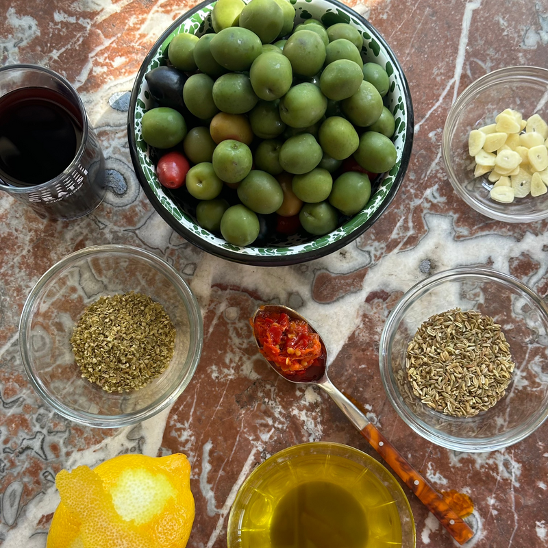 A bowl of olives and spices on a marble surface.