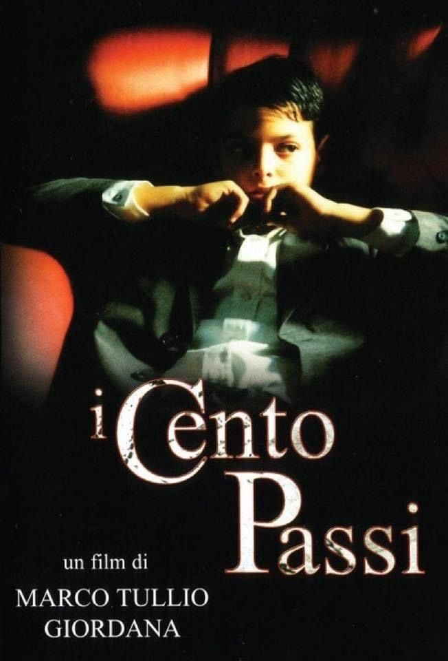 A young man sits pensively in a red chair with his hands near his face; dramatic lighting highlights his expression. Text reads I Cento Passi and un film di Marco Tullio Giordana.