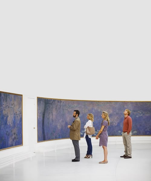 Four people stand side by side in a white, modern gallery, closely observing large, blue-toned abstract paintings displayed along a curved wall.