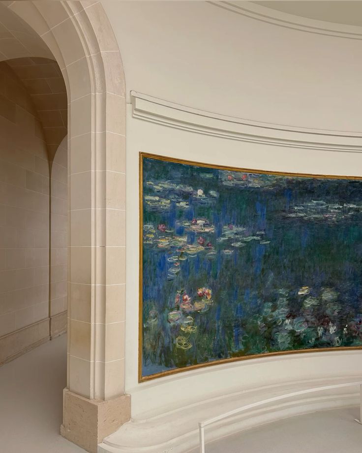A large Monet water lilies painting hangs on a curved, cream-colored wall in a bright, minimalist gallery with an arched doorway and smooth stone surfaces.