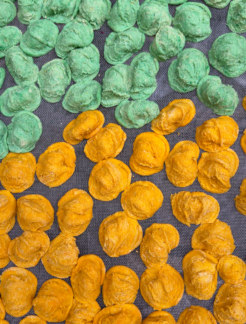 Rows of round, textured snacks in green and orange colors are arranged on a mesh surface, separated by color.