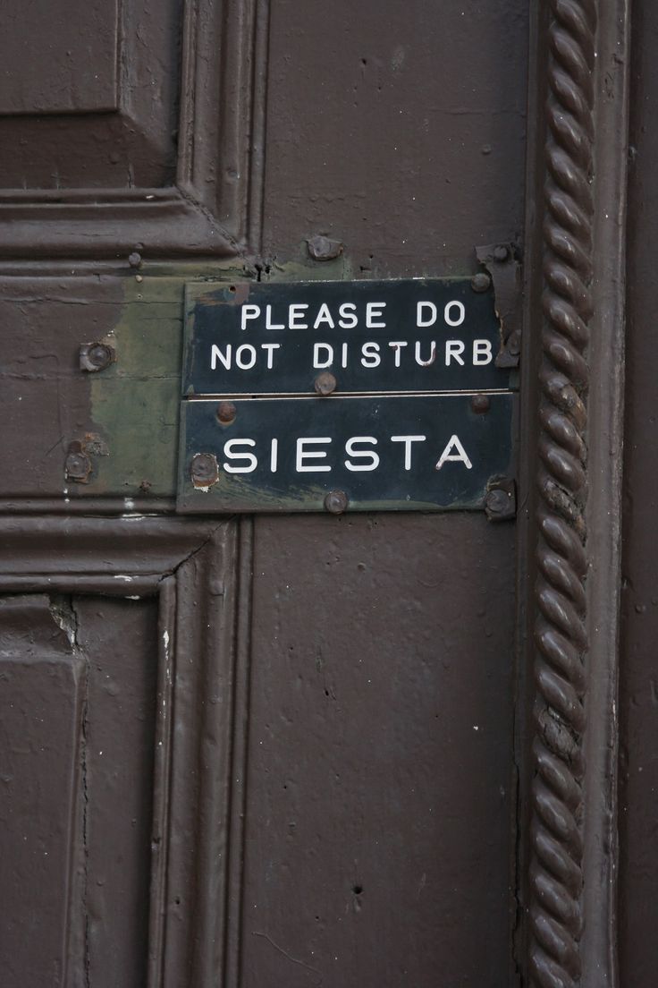 A close-up of a dark wooden door with a sign that reads, PLEASE DO NOT DISTURB SIESTA, indicating someone is resting inside.