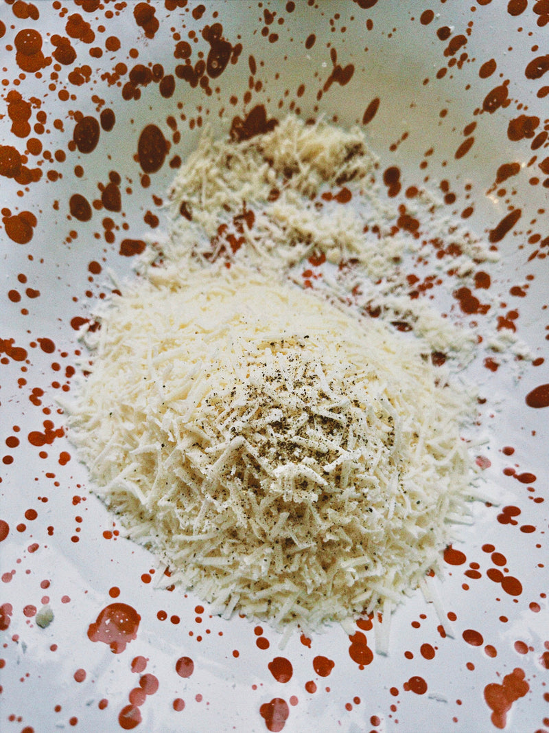 A close-up of grated cheese and ground black pepper on a white plate with red splatter patterns.