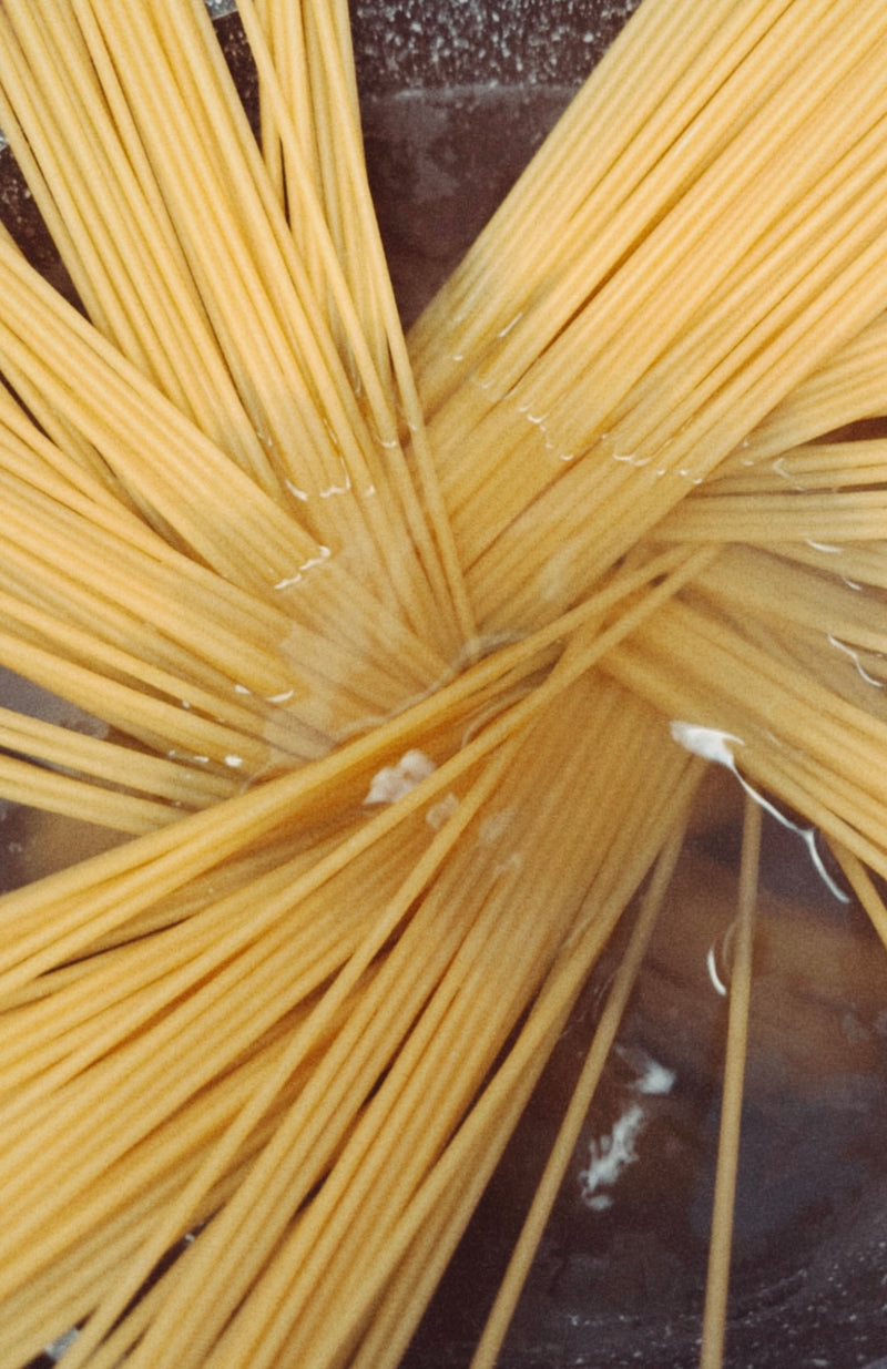 Uncooked spaghetti noodles are partially submerged in a pot of boiling water, with the noodles fanned out and beginning to soften as they cook.