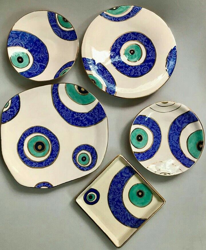 Five ceramic plates with bold, circular patterns in blue, green, black, and white, resembling evil eye designs, are arranged on a flat surface. The plates are of various shapes and sizes.