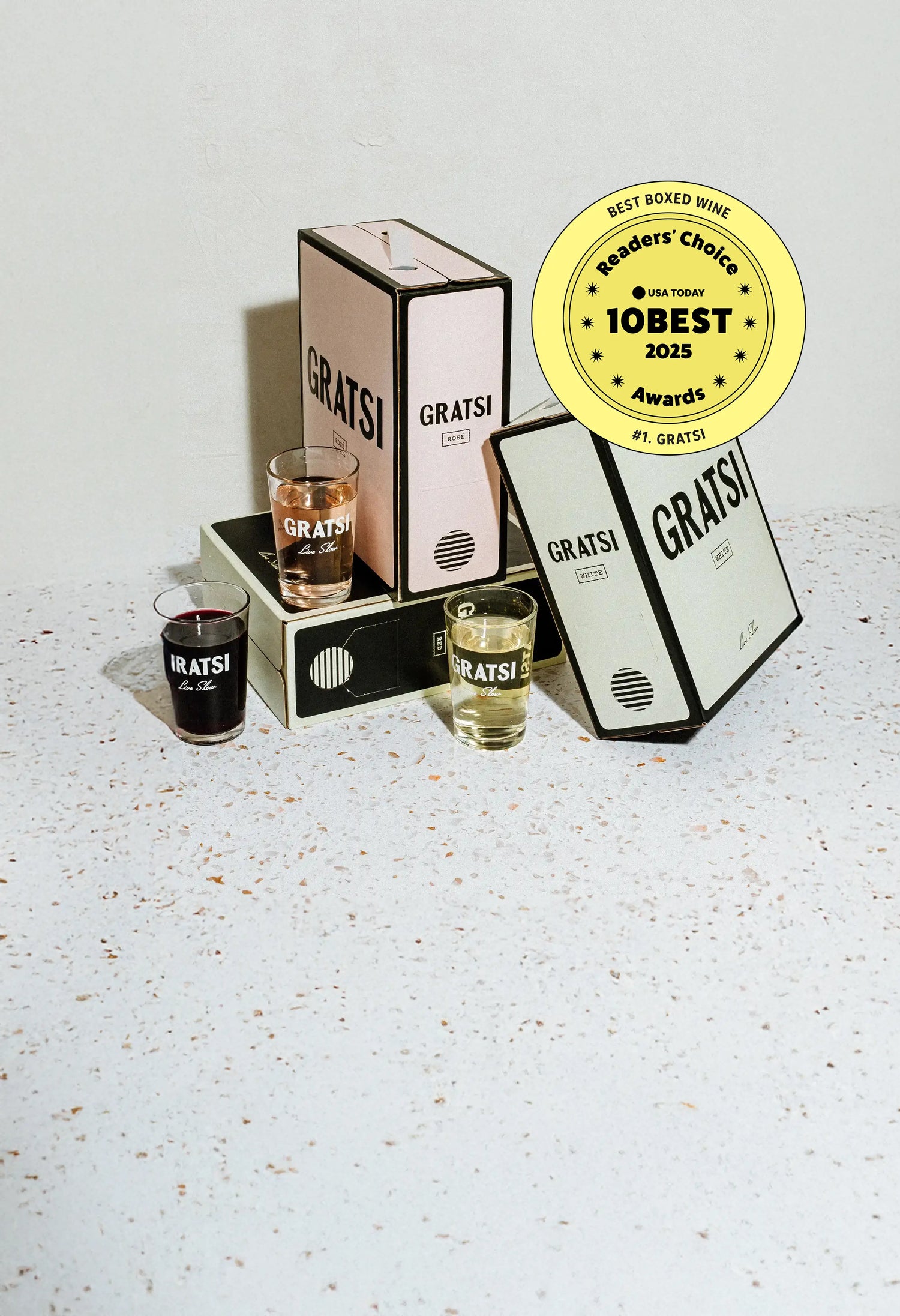 Three Gratsi boxed wines and three filled glasses are displayed on a speckled surface. A yellow USA Today 10Best Readers Choice 2025 Best Boxed Wine award badge is shown in the top right corner.