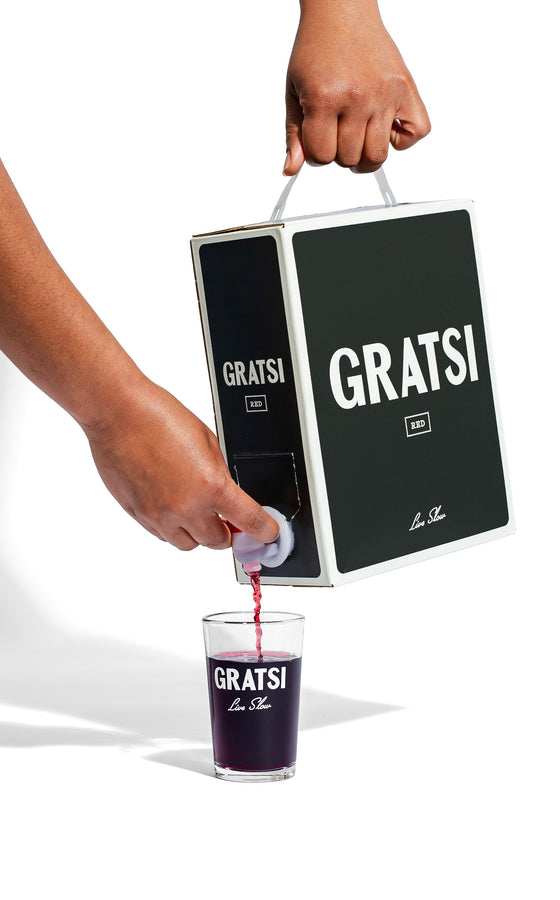 Someone pours Gratsi Red Wine from a sleek black box into a clear glass, both showing the Gratsi logo, set against a white background.