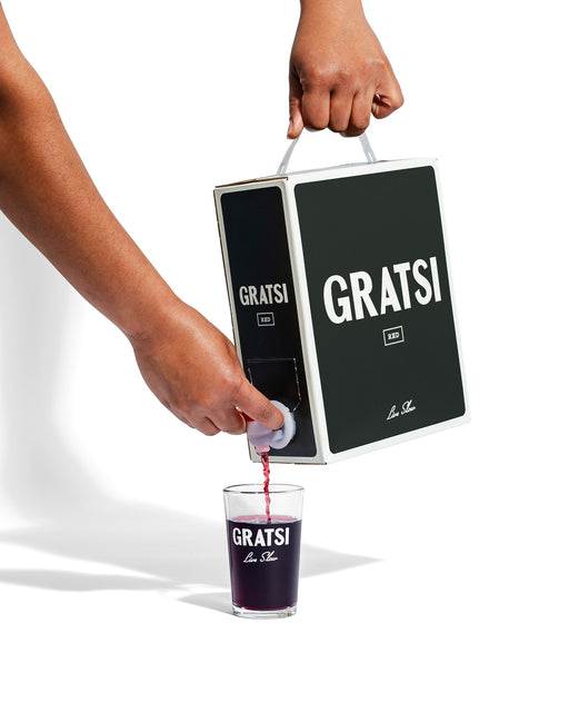Someone pours Gratsi Red Wine from a sleek black box into a clear glass, both showing the Gratsi logo, set against a white background.
