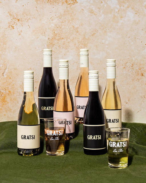 The Gratsi Wine Sampler Kit features 6 half bottles of zero-sugar wines in assorted colors with white caps, and 2 branded glasses, all arranged on a green cloth for an exclusive online gift set.