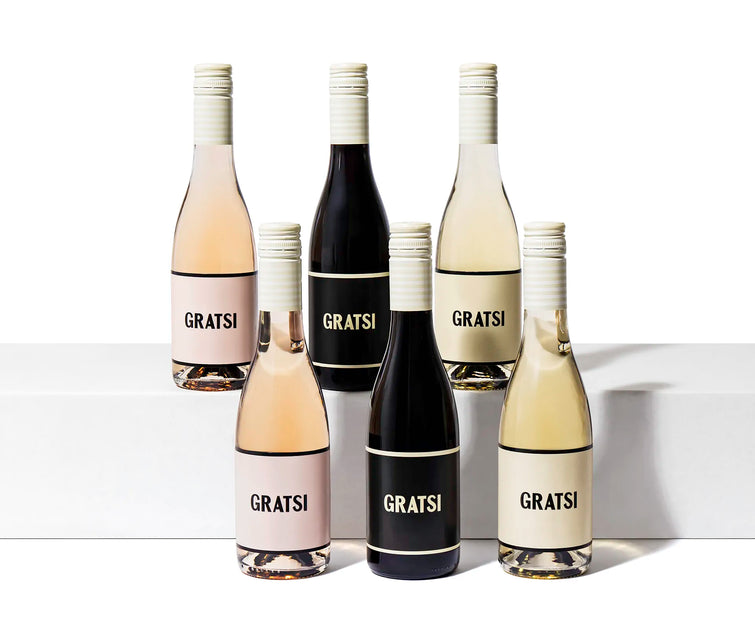 Six Gratsi half wine bottles and two glasses from the Wine Sampler Kit are displayed on white blocks, highlighting this exclusive zero-sugar online gift set.