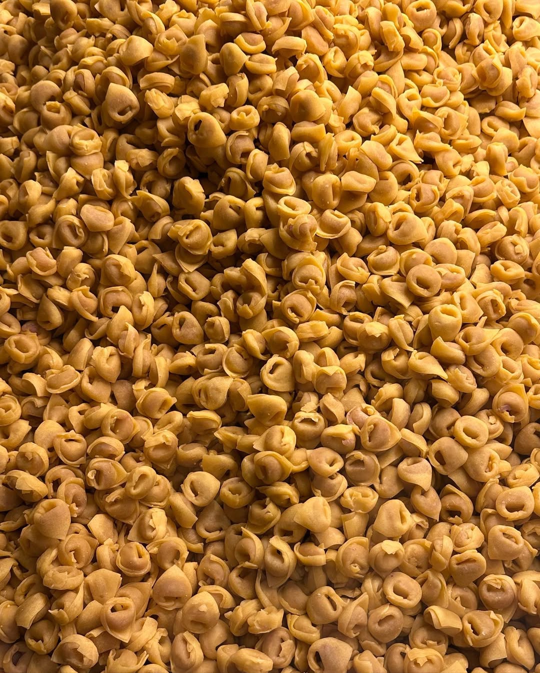 A large pile of uncooked tortellini pasta, closely packed together, creating a textured and uniform surface of small ring-shaped pasta pieces.