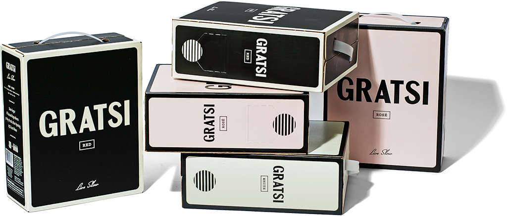 Five box-shaped wine containers labeled “GRATSI” in black, white, and pink designs are arranged in a staggered stack, some lying on their sides and one upright, with white handles visible on top.