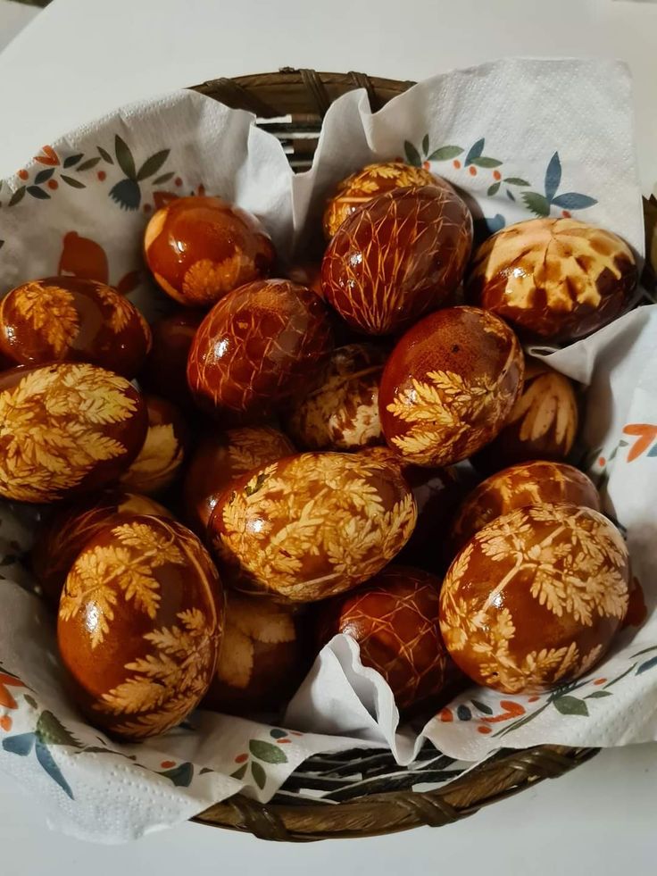 A basket lined with a decorative cloth holds several intricately decorated brown Easter eggs featuring natural leaf patterns and designs.