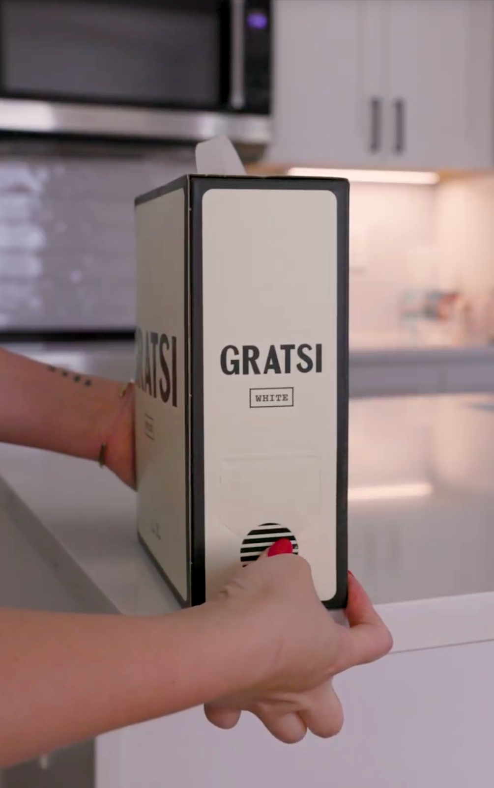 A person’s hands are holding a box of Gratsi white wine on a kitchen counter, with a modern kitchen in the background.