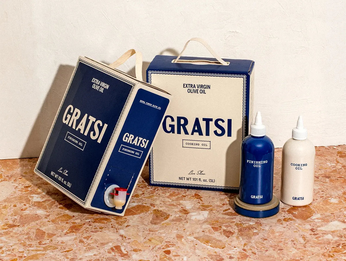 Two large rectangular boxes and two small squeeze bottles of Gratsi olive oil, with finishing oil in blue containers and cooking oil in beige containers.