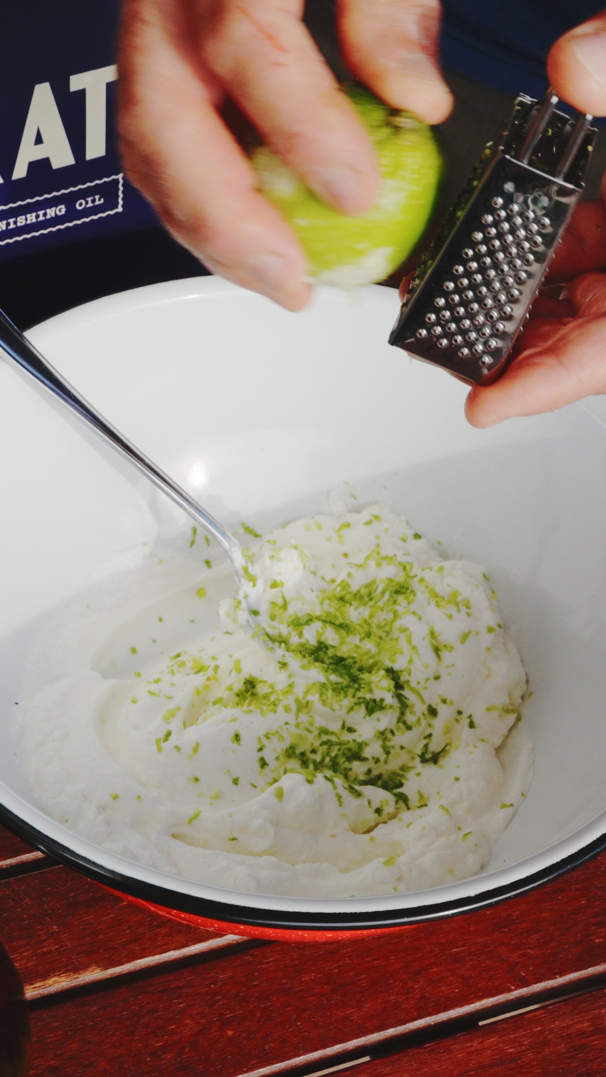 Hands grating a lime over a bowl of white cream.