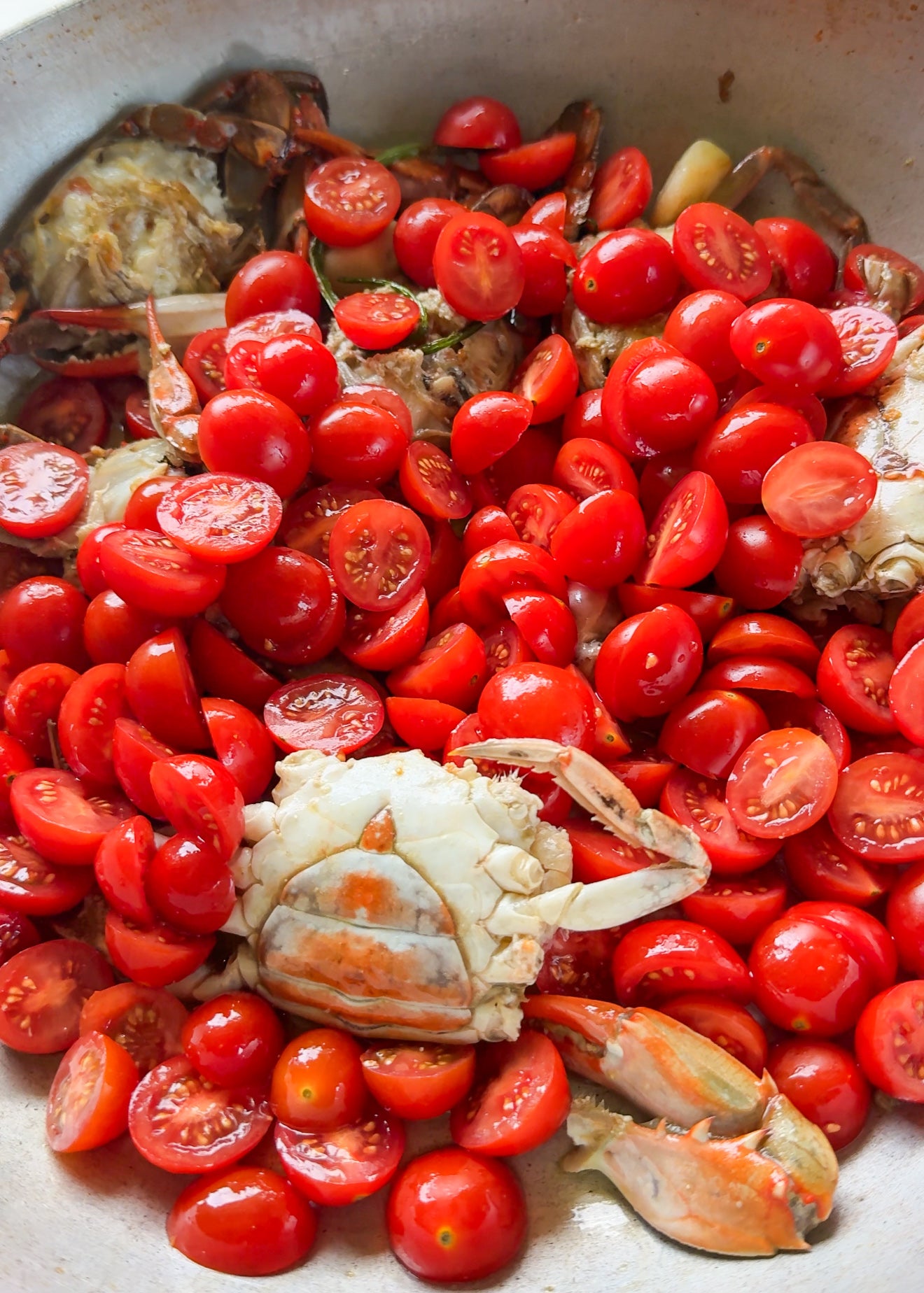 Fresh crabs with halved cherry tomatoes in a pan, ready to be cooked. The bright red tomatoes contrast with the pale crab shells.