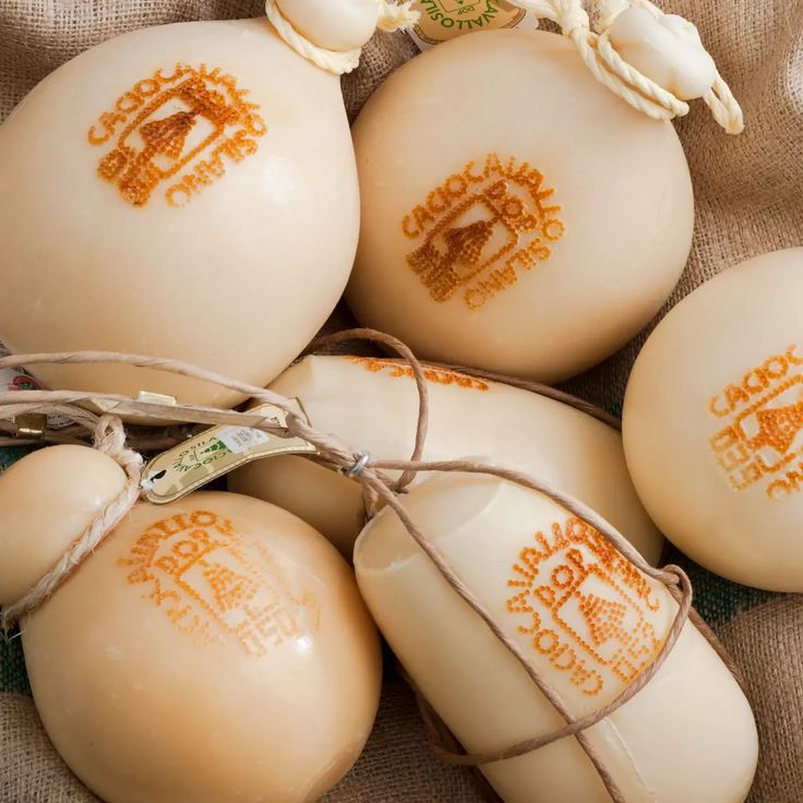 Several round, pale yellow cheeses with embossed labels reading Caciocavallo Podolico are tied with string and displayed together on a burlap surface.