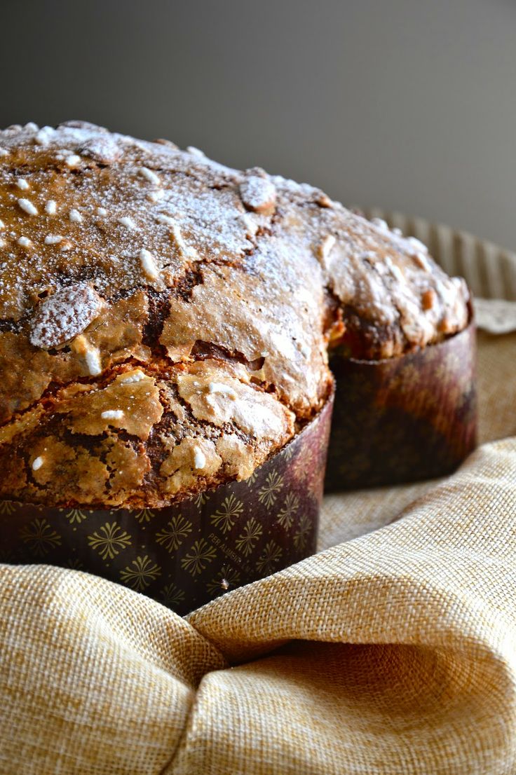 Close-up of two traditional Italian Easter breads (Colomba Pasquale) with a golden, crackled sugar and almond crust, wrapped in decorative paper and resting on a beige linen cloth.