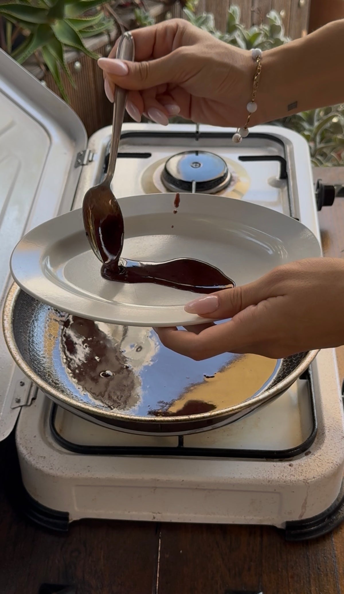 A person uses a spoon to drizzle dark liquid from a pan onto a small white plate.
