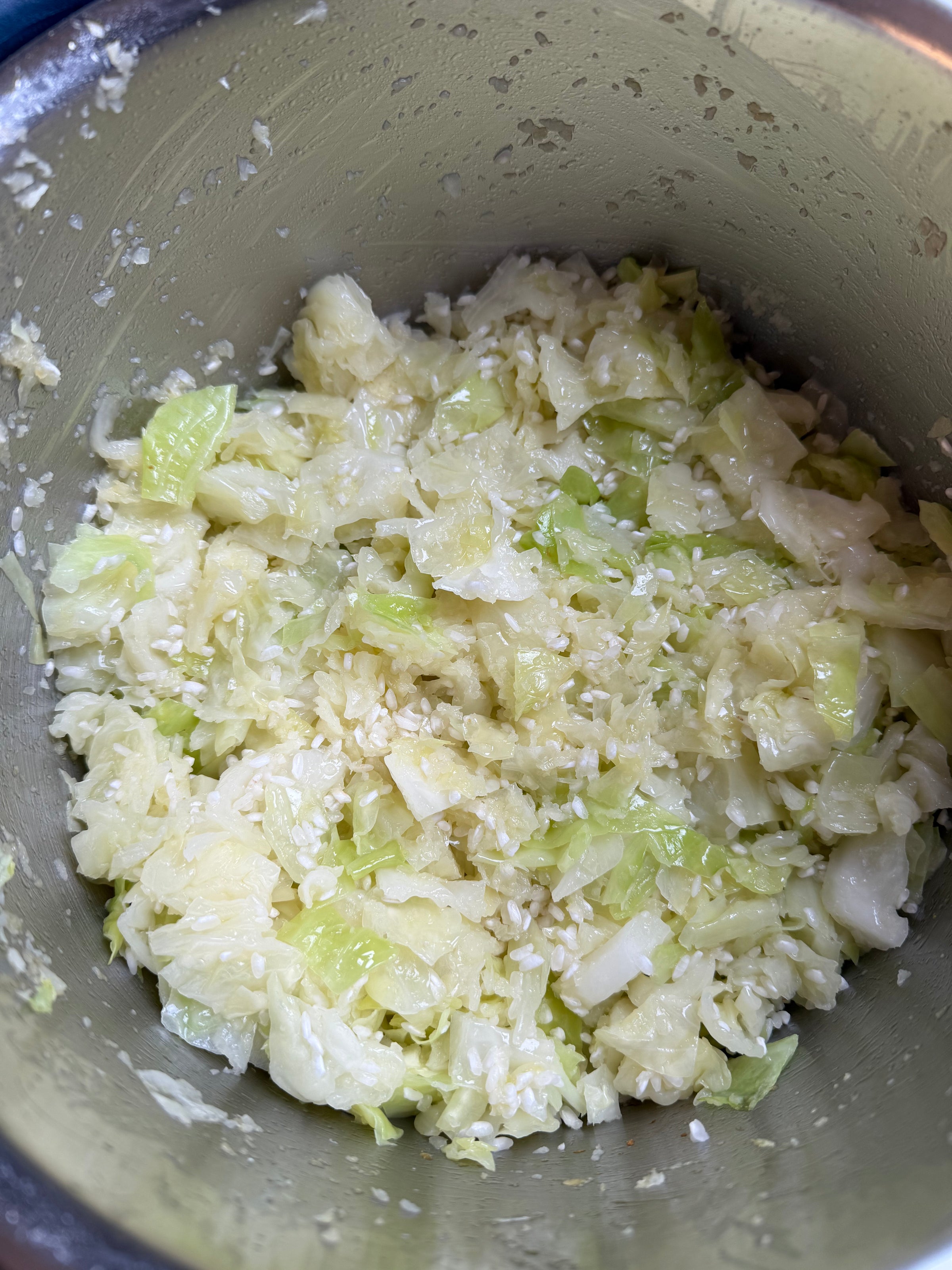 Chopped cabbage mixed with rice grains in a metal bowl, likely being prepared for a meal or recipe. The mixture appears fresh and lightly moist.