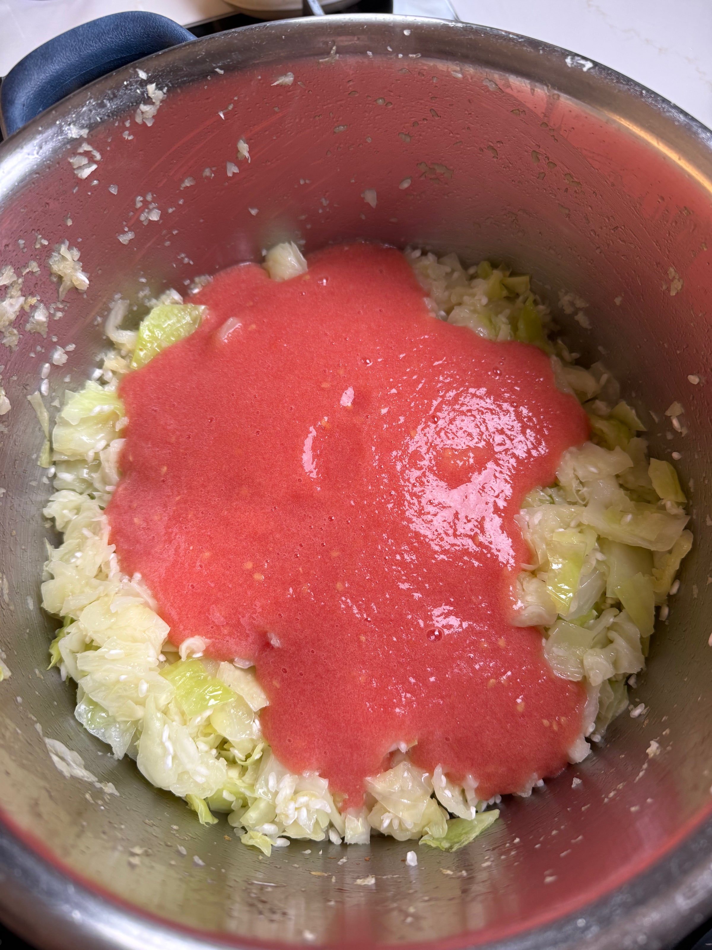 Chopped cabbage and onions are in a pot, topped with a layer of blended tomato sauce, ready to be cooked.