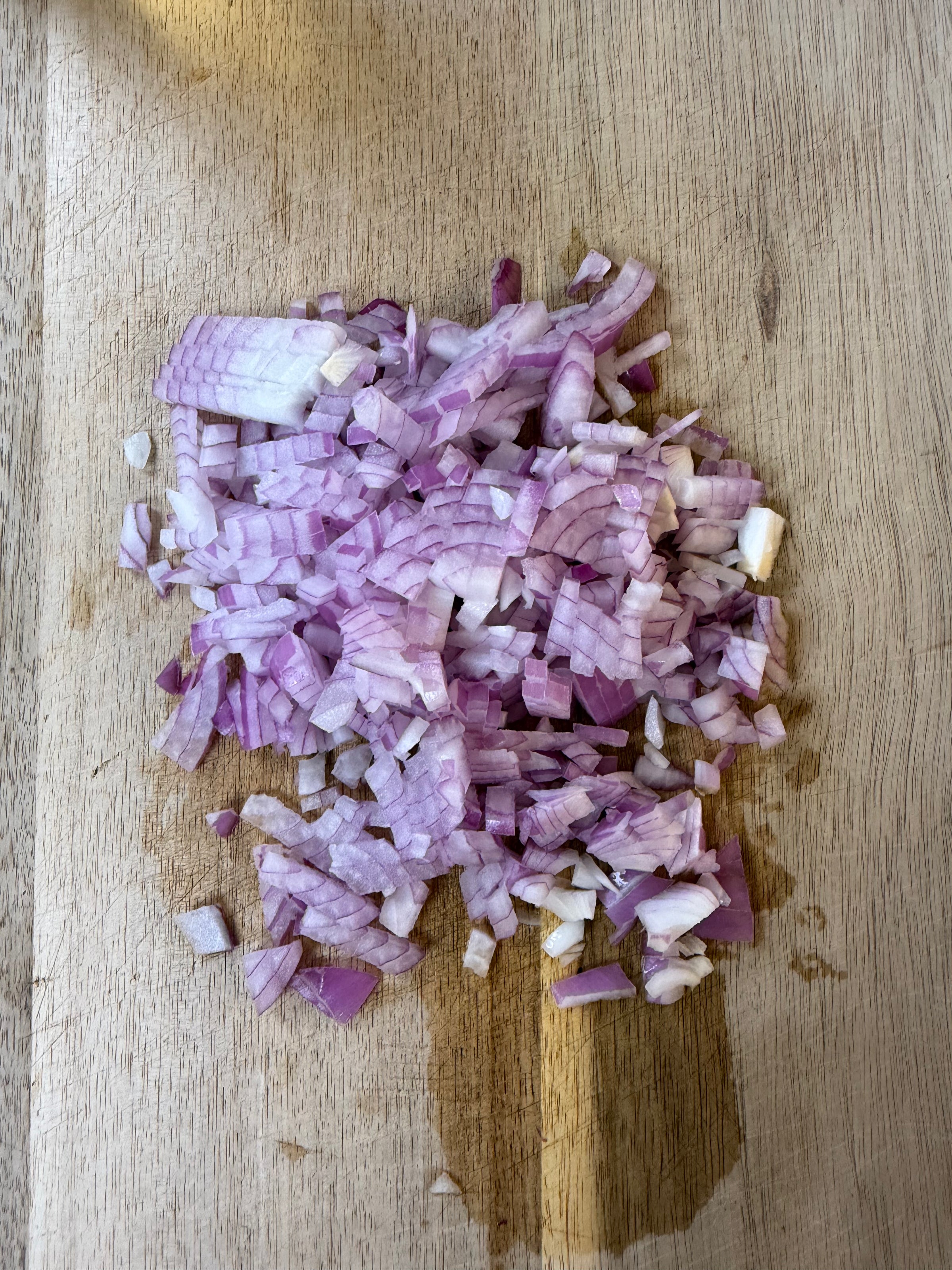 Finely chopped red onion pieces are spread out on a wooden cutting board.