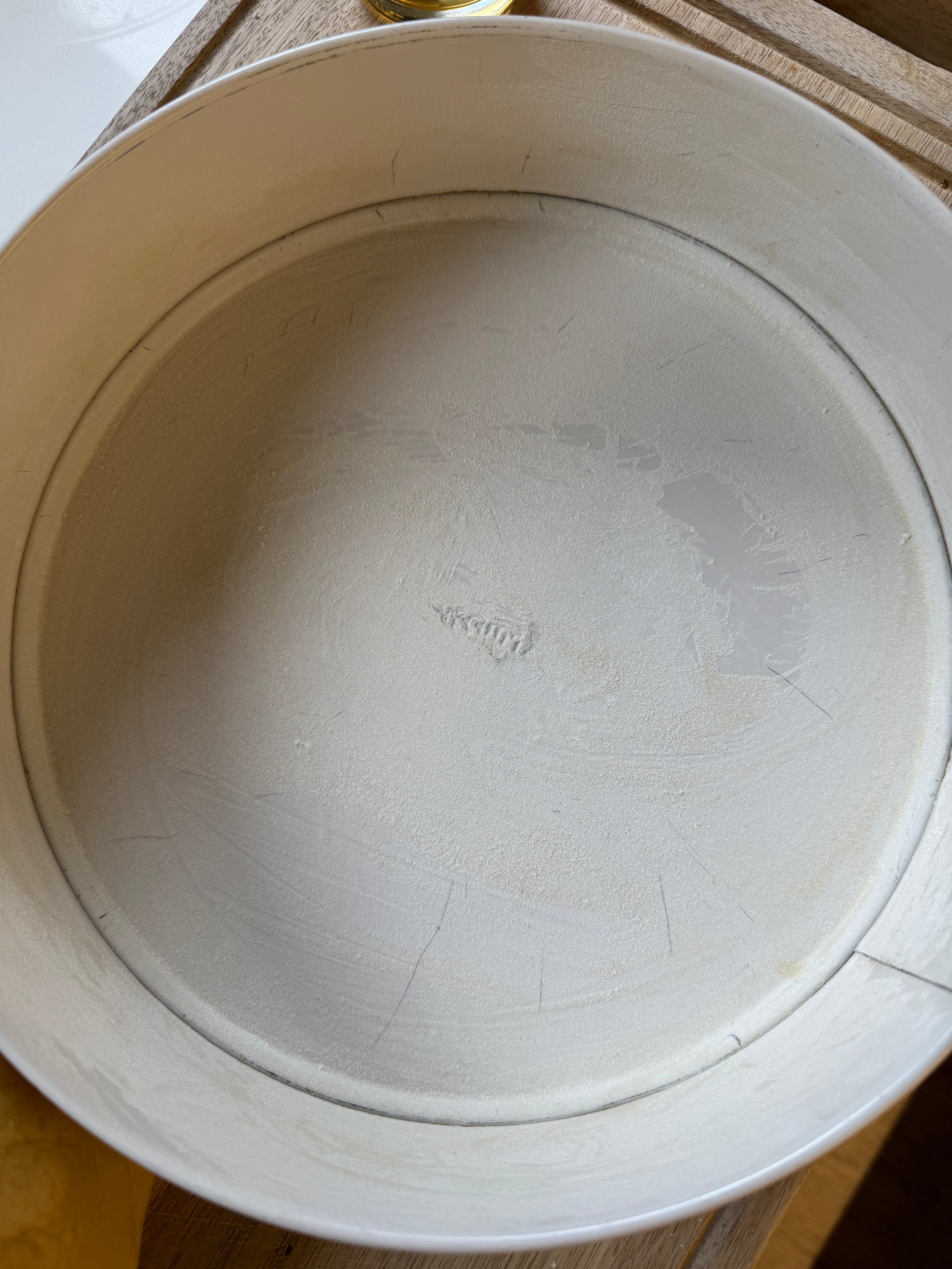 A close-up of a round metal cake pan with its interior evenly coated in flour, likely prepared for baking. The word “Focus” is faintly visible in the center of the pan’s base.