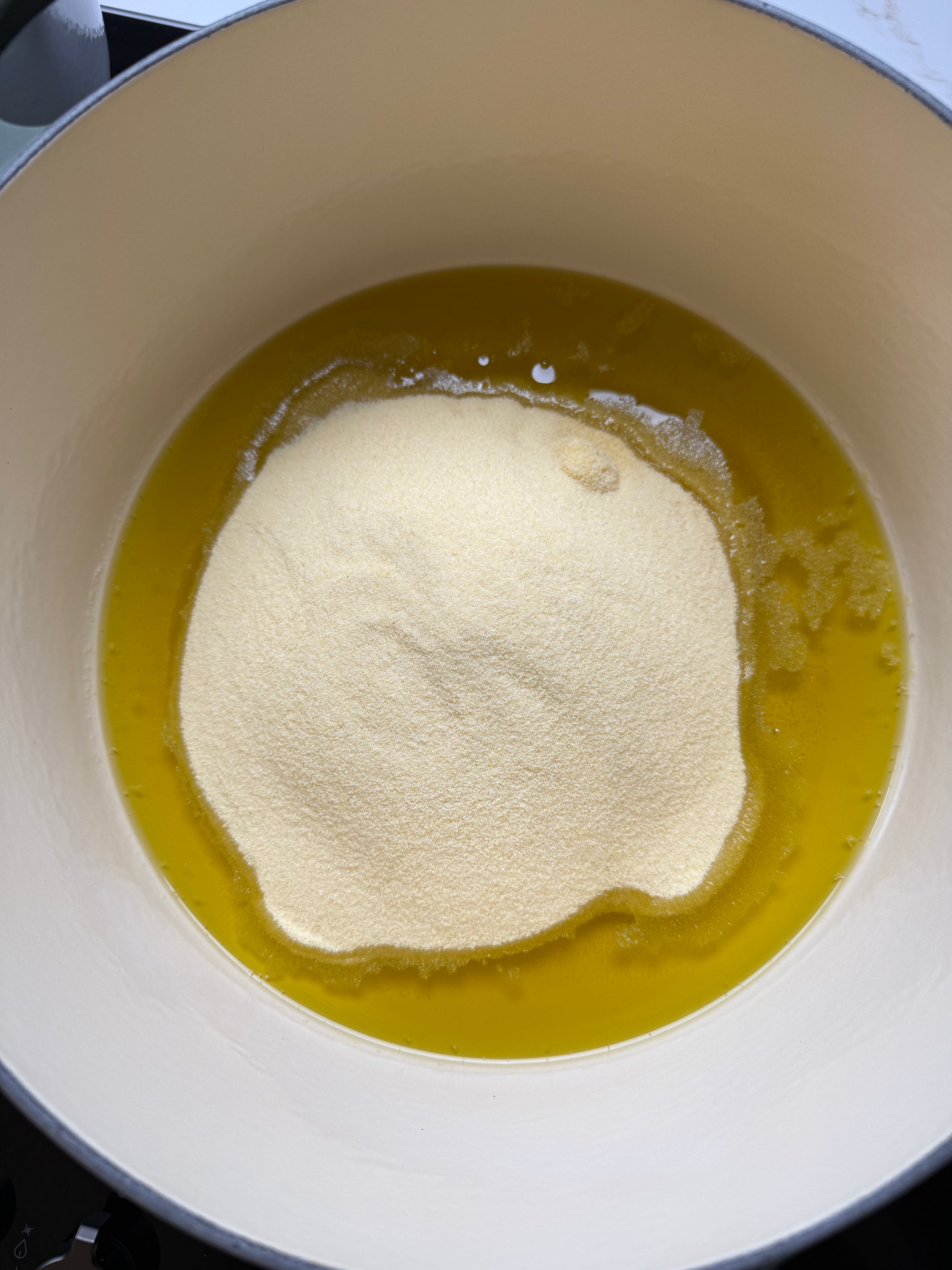 A mound of semolina sits on top of melted butter in a large white pot, ready for mixing.