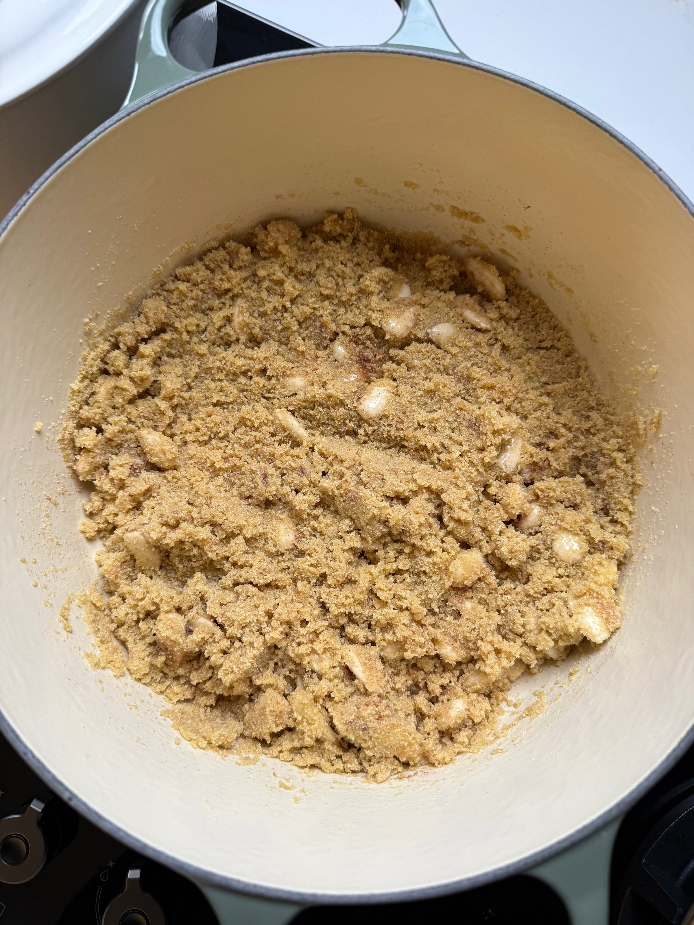 A close-up of a large white pot filled with a coarse, crumbly mixture of brown sugar and chunks of butter, likely being prepared for baking.