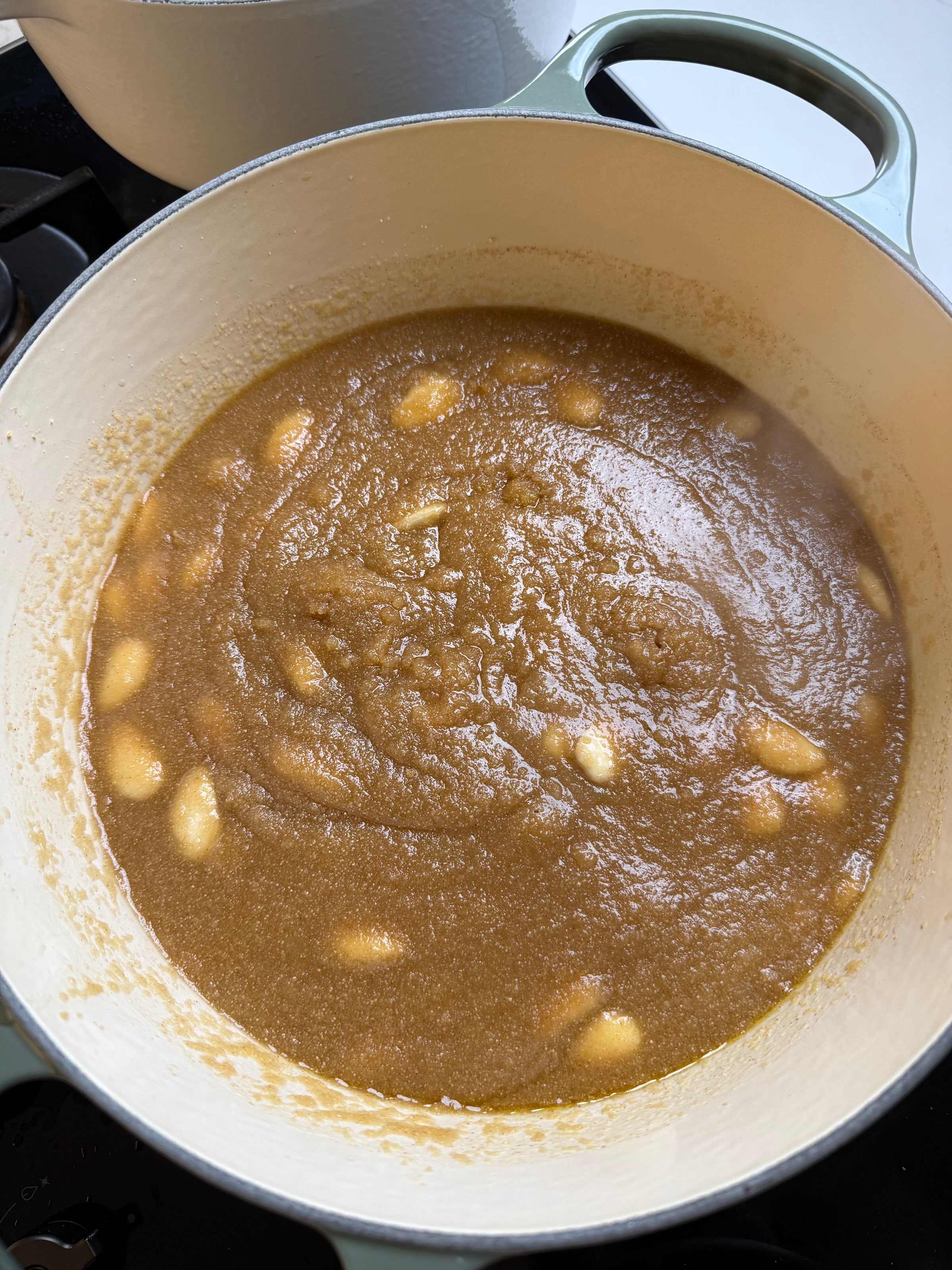 A pot filled with brown sauce or gravy, simmering and dotted with several whole garlic cloves. The sauce appears thick and smooth, with visible steam rising from it.