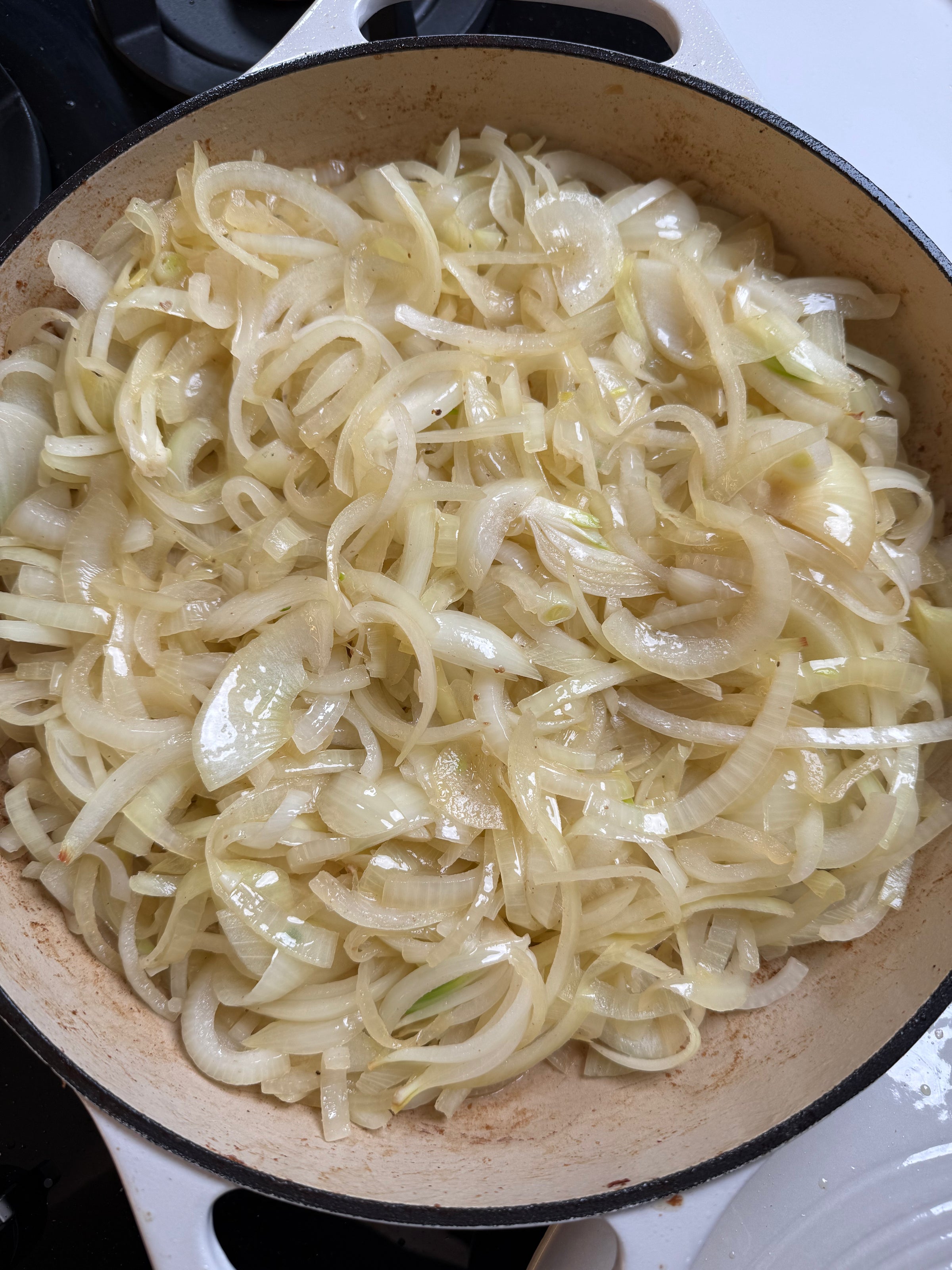 A large, light-colored pot filled with thinly sliced onions being sautéed, starting to turn translucent, on a stovetop.