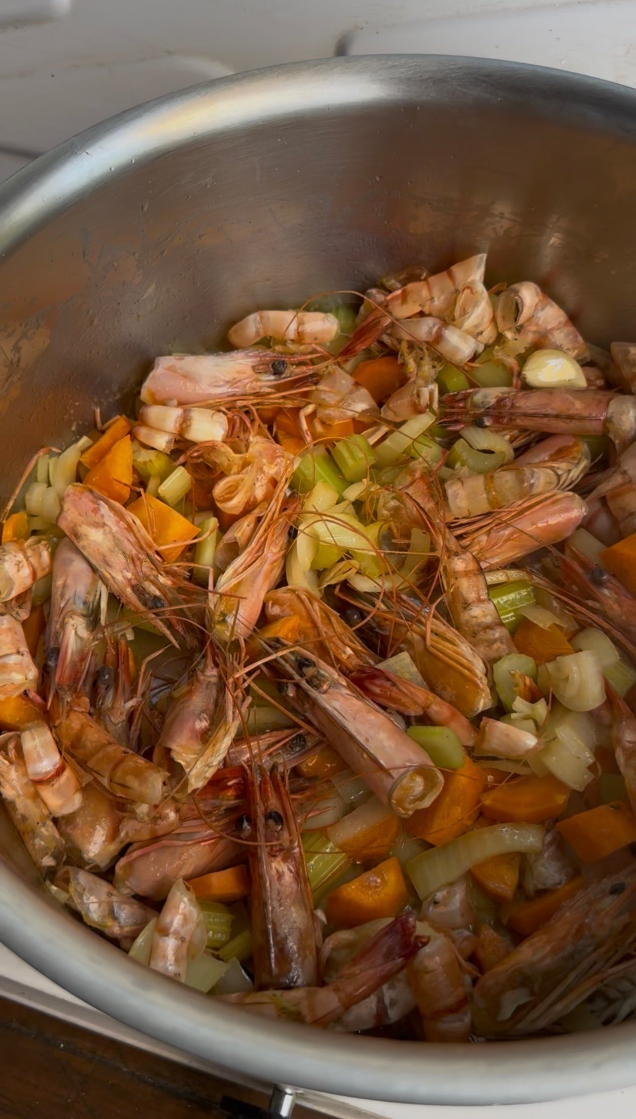 A pot filled with shrimp shells, chopped carrots, celery, and onions, showing the initial stages of making seafood stock.