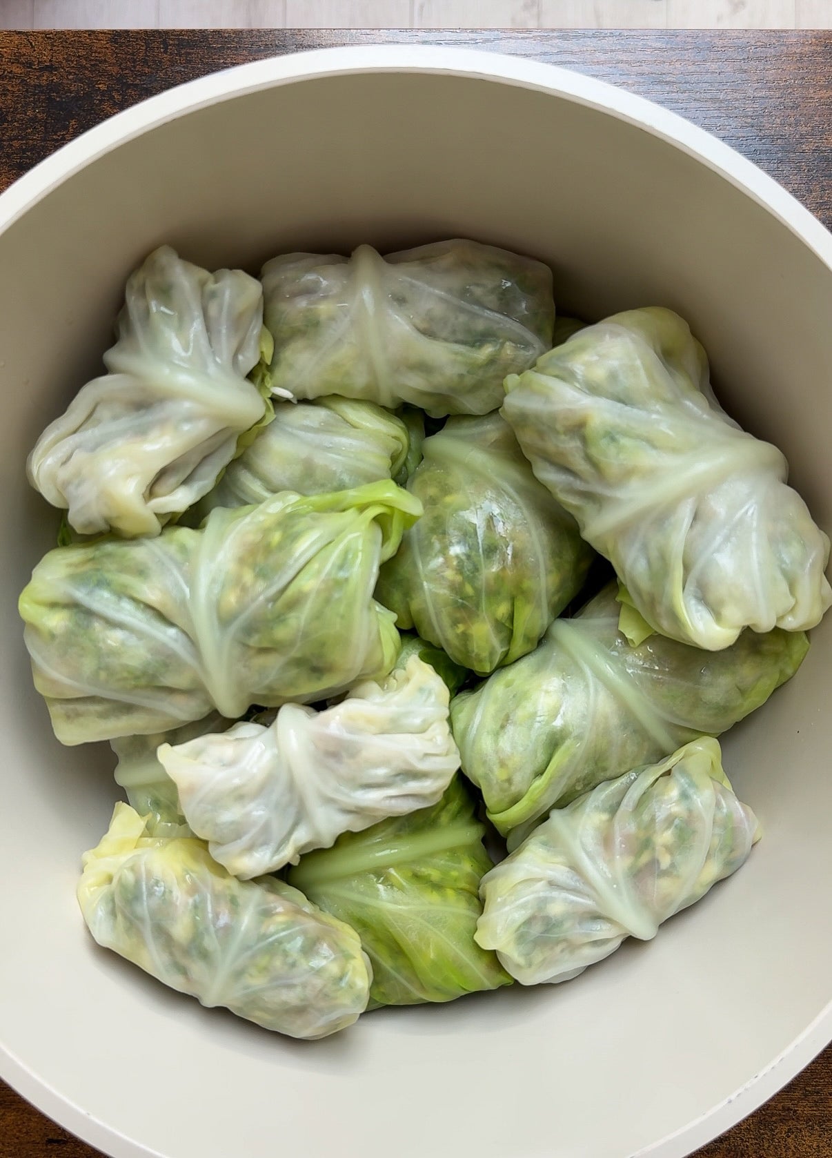 A bowl filled with neatly wrapped cabbage rolls, their green leaves tightly enclosing the filling, arranged in a single layer.
