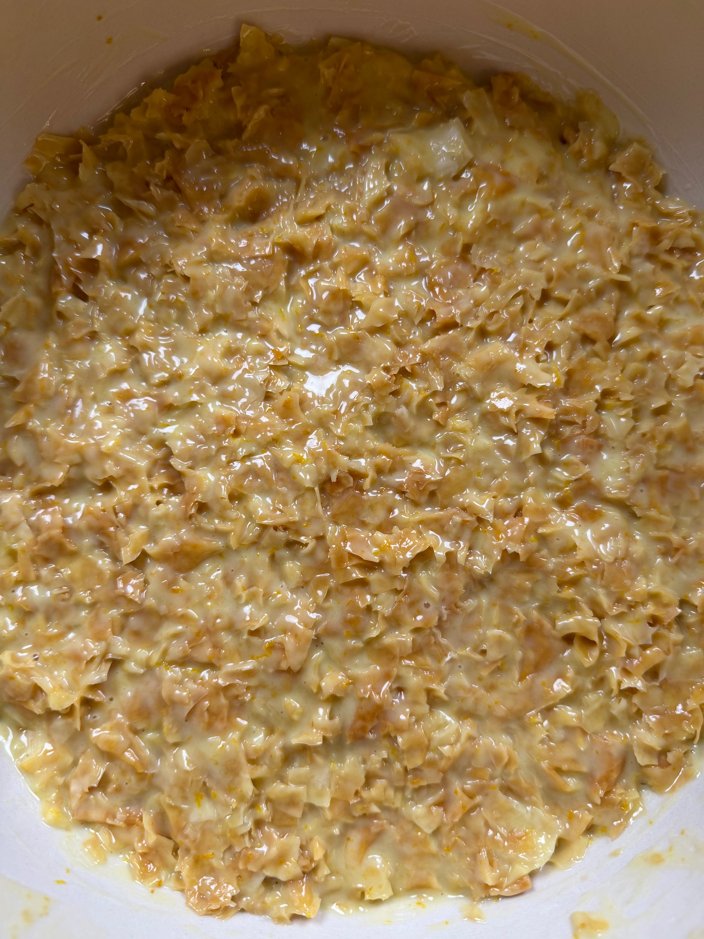 Close-up of a creamy, yellow-orange mixture with finely chopped pieces, possibly food like a cheesy casserole or a coleslaw in a bowl. The texture appears moist and chunky.